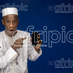 Jeune homme africain surpris, en tenue traditionnelle, montrant l'écran de son téléphone
