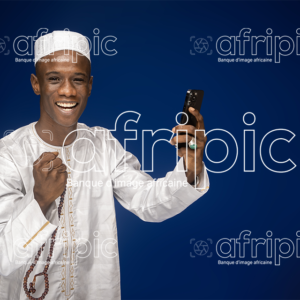 Jeune musulman africain souriant, en tenue traditionnelle, tenant un chapelet et un téléphone