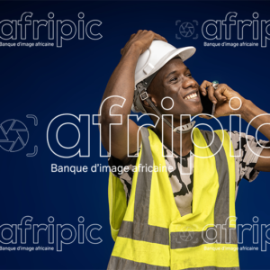 Jeune homme africain heureux en tenue de travaille, en communication téléphonique