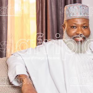Homme africain senior souriant, en tenue traditionnelle, assis dans son salon