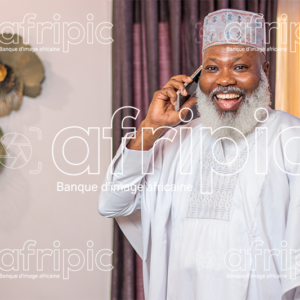 Homme africain senior , en communication téléphonique, dans son salon