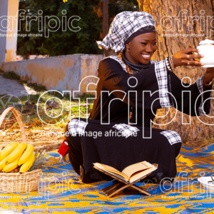 Jeune femme africaine en tenue traditionnelle toute souriante en période de Magal, assise à l'extérieur sur une natte