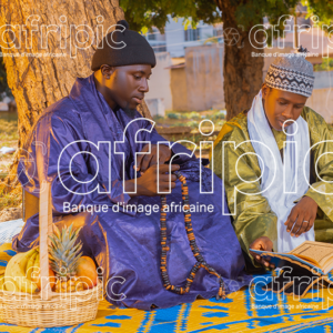 Jeunes africains en tenue traditionnelle, assis sur une natte à l'extérieur et lisant le coran.