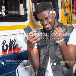 Jeune homme africain très heureux, en tenue moderne avec un téléphone à la main, devant un car rapide