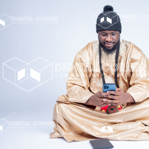 Jeune homme africain , assis en tenue traditionnelle, et manipulant son téléphone